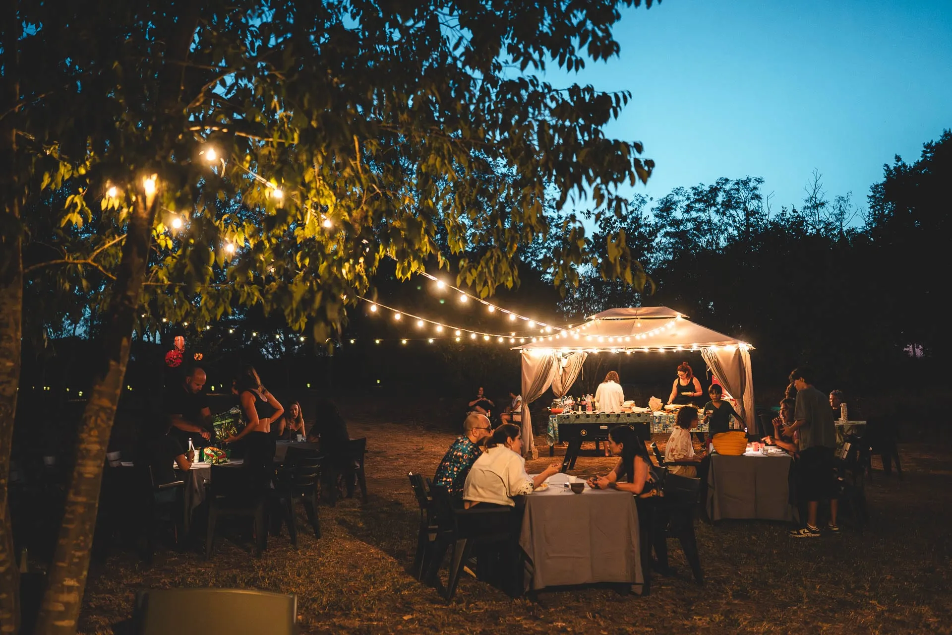 Una cena all'aperto all'imbrunire, con tavoli sotto le lucine e il gazebo