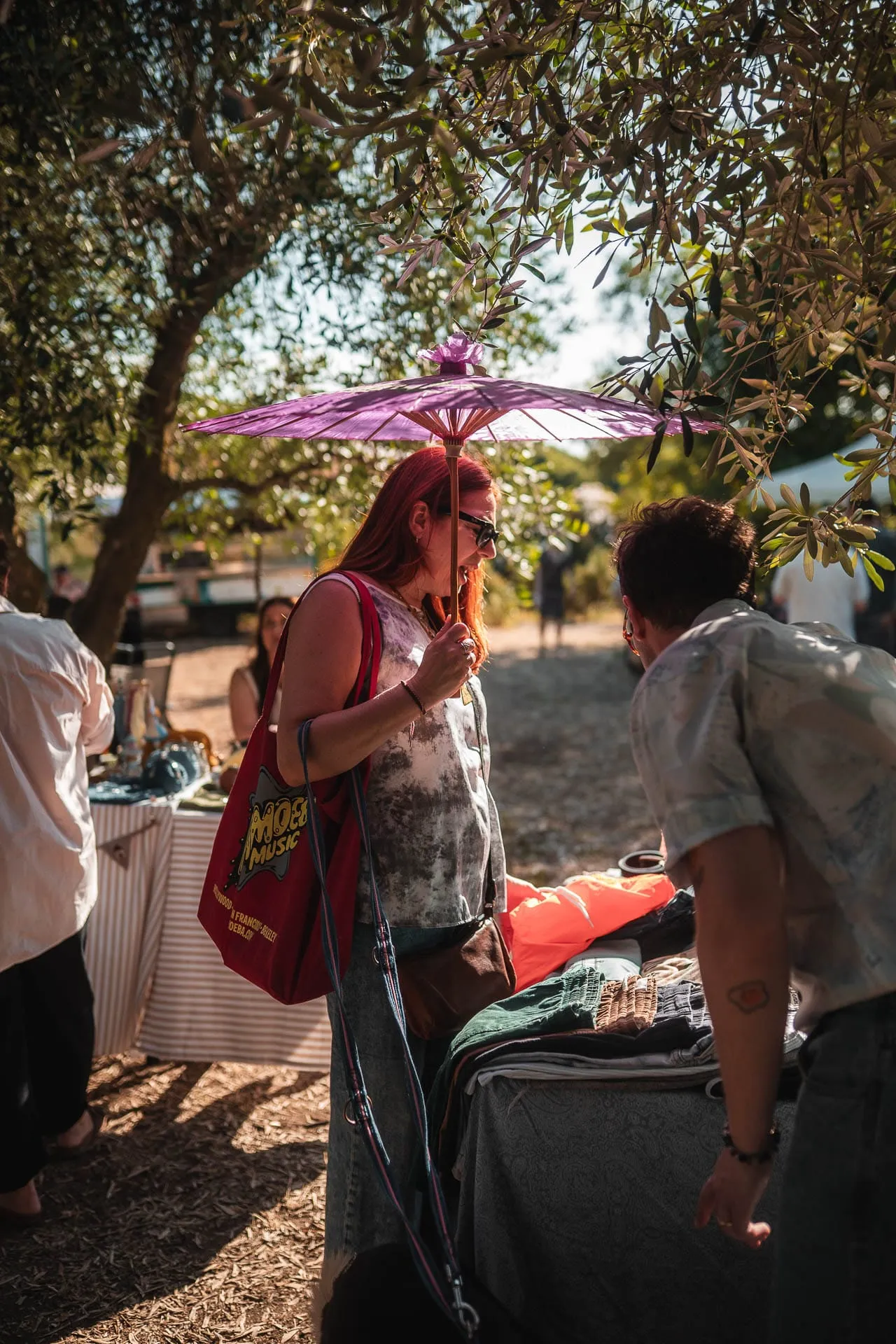 Visitors browsing the stalls in the afternoon sun, one with a parasol